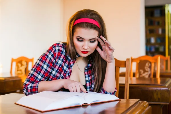 Clevere Studentin mit Pferdeschwanz sitzt mit Büchern in der Bibliothek. Innenräume — Stockfoto