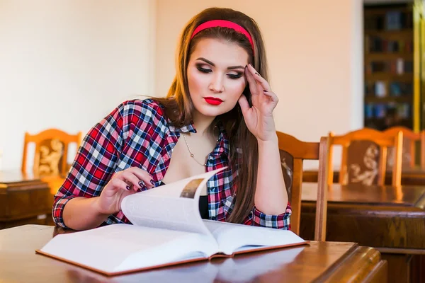 Clevere Studentin mit Pferdeschwanz sitzt mit Büchern in der Bibliothek. Innenräume — Stockfoto