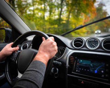 Sürücü koltuğu manzaralı. Direksiyonda el ele tutuşan adam, yakın plan. Ormanda yol