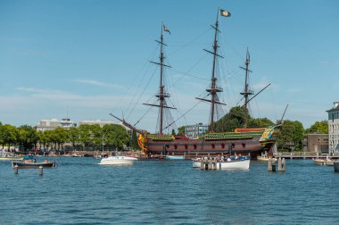 Amsterdam, Hollanda - 14 Temmuz 2025: Tarihi binalar ve botlar sıcak bir günbatımı gökyüzü altında sakin kanal sularına yansıdı.