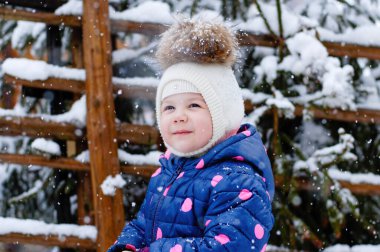 Açık havada mavi ceketli ve beyaz şapkalı küçük tatlı bir kızın portresi. Soğuk bir günde parkta kar ve karla oynayan sağlıklı, mutlu bir bebek. Çocuklar için şık kıyafetler.