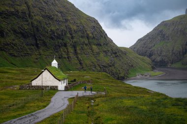 Faroe Adaları 'ndaki Saksun köyünün manzaralı manzarasında, yemyeşil bir vadiye yerleşmiş çim çatılı geleneksel evler yer alıyor. Yüksek kalite fotoğraf