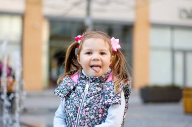 Sevimli Çocuk Mahalle Oyun Bahçesinde Güzel Zamanlar ve Maceralar Geçiriyor. Dilini gösteren sağlıklı, mutlu bir bebek. Çocuklar için şık kıyafetler.