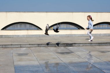 Sevimli Çocuk Mahalle Oyun Bahçesinde Güzel Zamanlar ve Maceralar Geçiriyor. Güvercinlerle koşan sağlıklı, mutlu bir bebek. Çocuklar için şık kıyafetler.