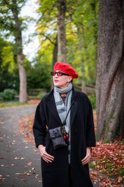 Şık, bakımlı, şık bir kadın bulutlu bir günde bir sonbahar parkında yürüyor. Kırmızı bereli, kırmızı rujlu, kendine güvenen ve sofistike görünen aynı kırmızı taytı giyiyor..