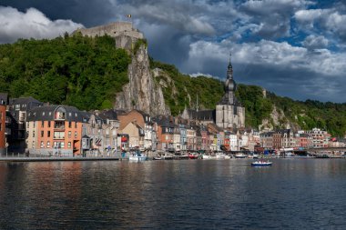 Belçika 'nın Dinant kentinin manzarasında, tarihi nehir kenarı binaları ve Meuse Nehri' nin üzerinde tünemiş kale bulunuyor..