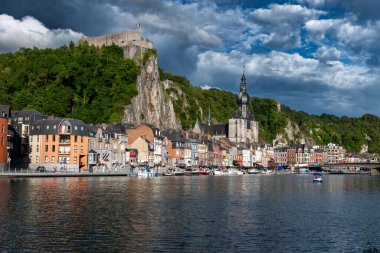 Belçika 'nın Dinant kentinin manzarasında, tarihi nehir kenarı binaları ve Meuse Nehri' nin üzerinde tünemiş kale bulunuyor..