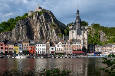 Belçika 'nın Dinant kentinin manzarasında, tarihi nehir kenarı binaları ve Meuse Nehri' nin üzerinde tünemiş kale bulunuyor..