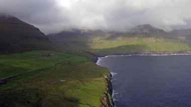 Faroe Adaları 'nın dramatik yeşil uçurumları, kayalık kıyı şeridi ve bulutlu kuzey havası altındaki okyanus dalgalarıyla manzarası. Nordladalur 'un sert ve el değmemiş doğası.