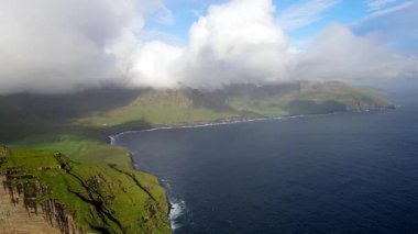 Faroe Adaları 'nın dramatik yeşil uçurumları, kayalık kıyı şeridi ve bulutlu kuzey havası altındaki okyanus dalgalarıyla manzarası. Nordladalur 'un sert ve el değmemiş doğası.