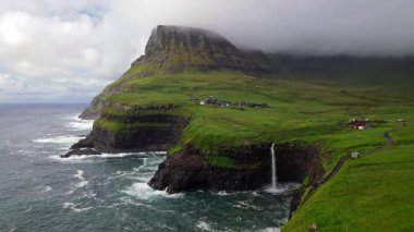 Dramatik Mulafossur şelalesi Gasadalur köyü ve arka planda kayalıklarla okyanusa dökülüyor..