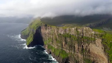 Faroe Adaları 'nın dramatik yeşil uçurumları, kayalık kıyı şeridi ve bulutlu kuzey havası altındaki okyanus dalgalarıyla manzarası. Nordladalur 'un sert ve el değmemiş doğası.