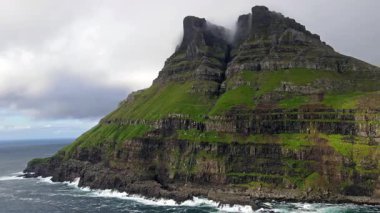 Faroe Adaları 'nın dramatik yeşil uçurumları, kayalık kıyı şeridi ve bulutlu kuzey havası altındaki okyanus dalgalarıyla manzarası. Nordladalur 'un sert ve el değmemiş doğası.