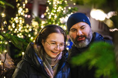 Gülümseyen kız ve babası sıcacık bir bayram ortamı yaratan parıldayan Noel ışıklarıyla çevrili sıcak bir anın tadını çıkarıyorlar..