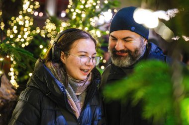 Gülümseyen kız ve babası sıcacık bir bayram ortamı yaratan parıldayan Noel ışıklarıyla çevrili sıcak bir anın tadını çıkarıyorlar..
