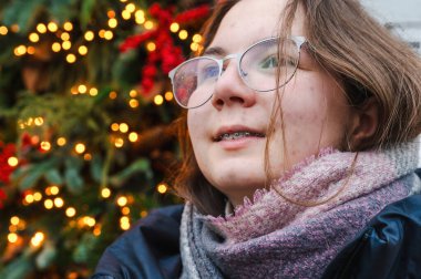 Sıcak tatil ışıklarıyla aydınlatılan gülümseyen kız neşeli ve rahat bir Noel atmosferi yaratıyor..