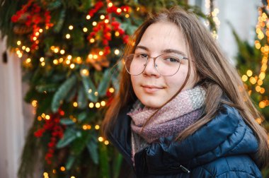 Sıcak tatil ışıklarıyla aydınlatılan gülümseyen kız neşeli ve rahat bir Noel atmosferi yaratıyor..