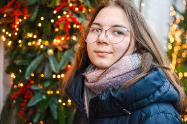 Sıcak tatil ışıklarıyla aydınlatılan gülümseyen kız neşeli ve rahat bir Noel atmosferi yaratıyor..