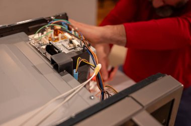 Odaklanmış olgun bir adam bozuk bir elektronik cihazı tamir eder. Röleleri ve çipleri hassasiyetle değiştirir. Detaylı onarım için küçük aletler kullanır..