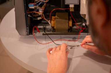 Odaklanmış olgun bir adam bozuk bir elektronik cihazı tamir eder. Röleleri ve çipleri hassasiyetle değiştirir. Detaylı onarım için küçük aletler kullanır..