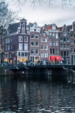 Amsterdam, Hollanda - 3 Ocak 2026: Tarihsel binalar ve botlar, kışın gökyüzü altında sakin kanal sularına yansıdı.