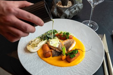 Lüks bir restoran ortamında altın garnitürlü balık yemeğinin şık sunumu.