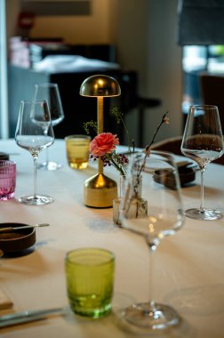 Pirinç lamba ve cam kaplama ile zarif masa ayarları, yeşil bardak ve beyaz keten üzerinde pembe çiçek, cilalı