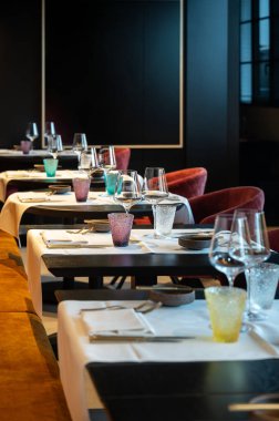 Renkli cam eşyalar ve kadehlerle sıralanmış masalar, siyah masa üstleri, katlanmış peçeteler, minimal sofra takımı.,