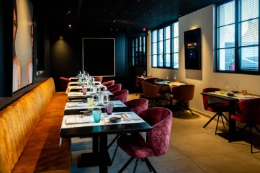Kadife sandalyeler, uzun ziyafet ve çerçeveli sanat eserleri ve düşük kalorili ışıklandırmayla servis edilen çevre yemek odası.