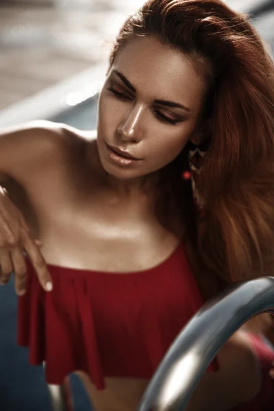 Retrato de uma linda menina bronzeada em um maiô com uma esfregona de cabelo vermelho que está posando ao ar livre na piscina — Fotografia de Stock