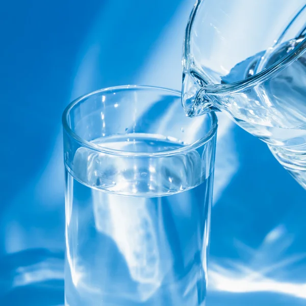Glass of water with a jug on a blue background — Stock Photo, Image
