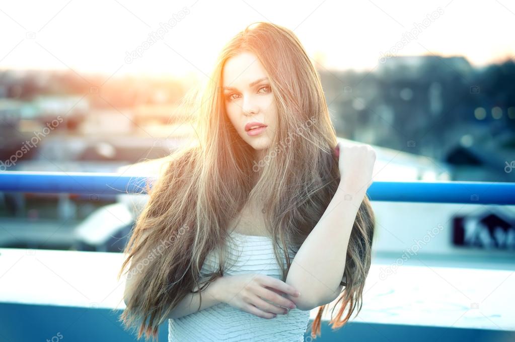 Pretty sexy woman with sensual lips posing at roof at the end of bright sunset.