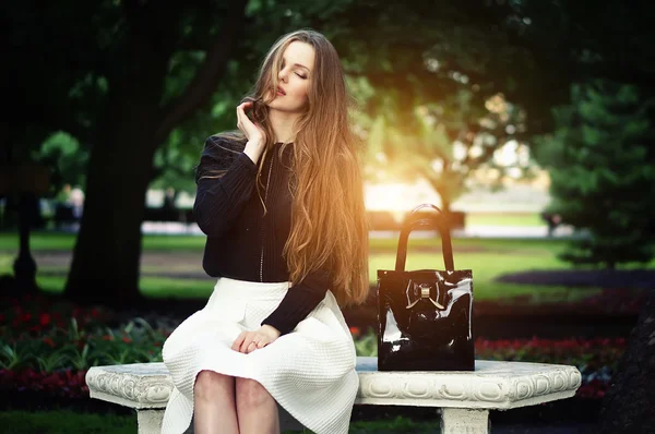 Frau sitzt auf der Bank und genießt die Natur an sonnigen Tagen im Freien. Stockbild