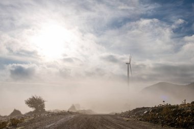 Bir rüzgar türbini dağın tepesindeki bir rüzgâr çiftliğinde şafak vakti kısmen sisle kaplı..