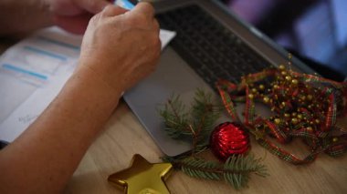 İnternette kredi kartı ekstrelerini ödemek için banka kartı kullanan ve masasında Noel süsleri olan birinin yakın plan fotoğrafı. Noel kredisi, Noel konsepti maliyeti.