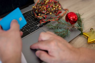 Noel harcamaları, finansal maliyet konsepti. Banka kartı kullanarak çevrim içi fatura ödemesi yapan bir kişi. Etrafta Noel süslerinden arta kalan parçalar var..
