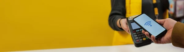 Müşteri, NFC teknolojisini kullanarak akıllı telefon ile ödeme yapıyor. Ödeme terminali ve satıcının kızı ile karşılaştırıldığında,