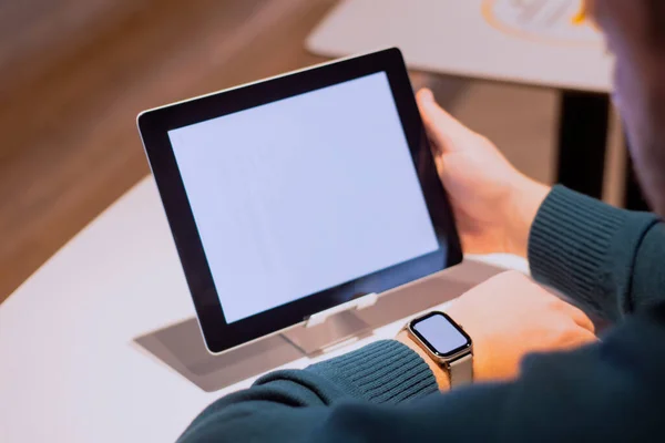 Businessman with digital tablet with white screen on the table and smart watch on his hand. A male freelancer works in a cafe