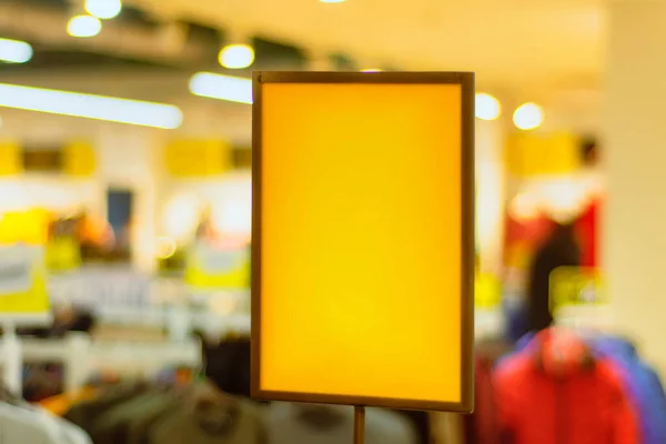 Yellow paper mockup of a discount signboard on the background of a store with clothes