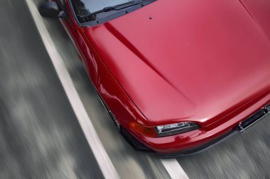 Kırmızı spor araba yüksek hızda hareket ediyor. Yukarıdan görüntüle, yolun arka planına karşı taşıma