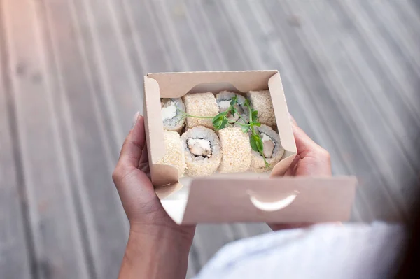 The girl opens a cardboard bag with a set of sushi. Seafood delivery concept
