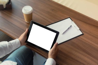 Elinde dijital tablet bulunan beyaz gömlekli bir işadamı ofiste bir sözleşme imzalıyor. Bir fincan kahve ve ahşap bir masa üzerindeki kalemli bir belge ile işyeri.
