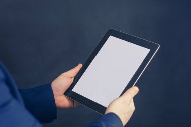Mavi ceketli bir iş adamı, siyah arka planda beyaz ekranlı bir tabletin bir kopyasını elinde tutuyor.