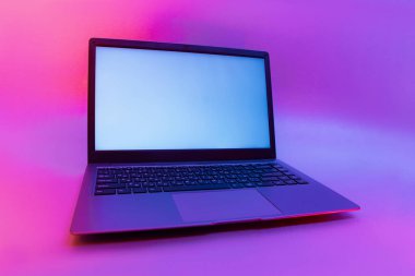 Arka planda beyaz ekran yaratıcı ışığı olan ince modern bir laptop. Renkli parlak neon, mavi ve mor ışıklarda bir model.