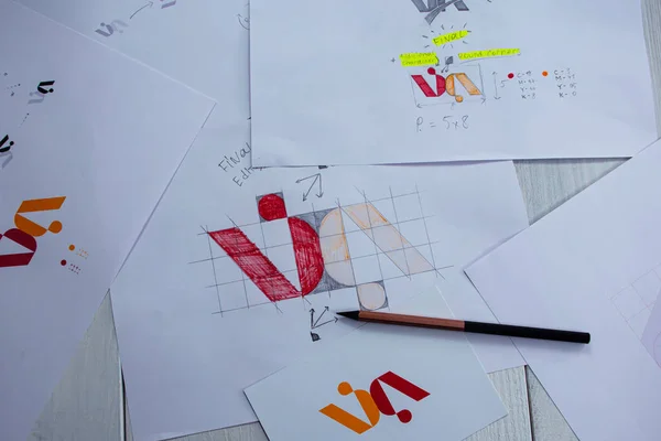 Sketches and drawings of the logo printed on paper. Development of logo design in the studio on a table