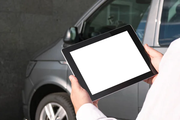 Mock up technology. Businessman in a white shirt holds a tablet with a white screen on the background of a minibus