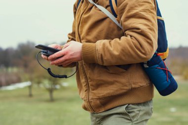 Turist elinde akıllı bir telefonla taşınabilir bir şarj aleti tutuyor. Doğanın arka planında yeşillik olan bir adam.