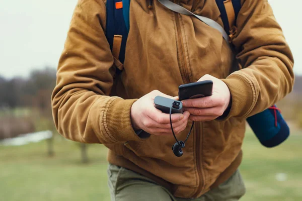 Tourist is holding a portable charger with a smartphone in his hand. Man on a background of nature with greens