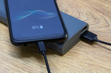 Taşınabilir şarj aleti ahşap bir masada akıllı telefonu şarj ediyor. Telefon ve kablolu güç bankası