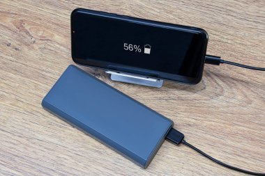 Taşınabilir şarj aleti ahşap bir masada akıllı telefonu şarj ediyor. Telefon ve kablolu güç bankası